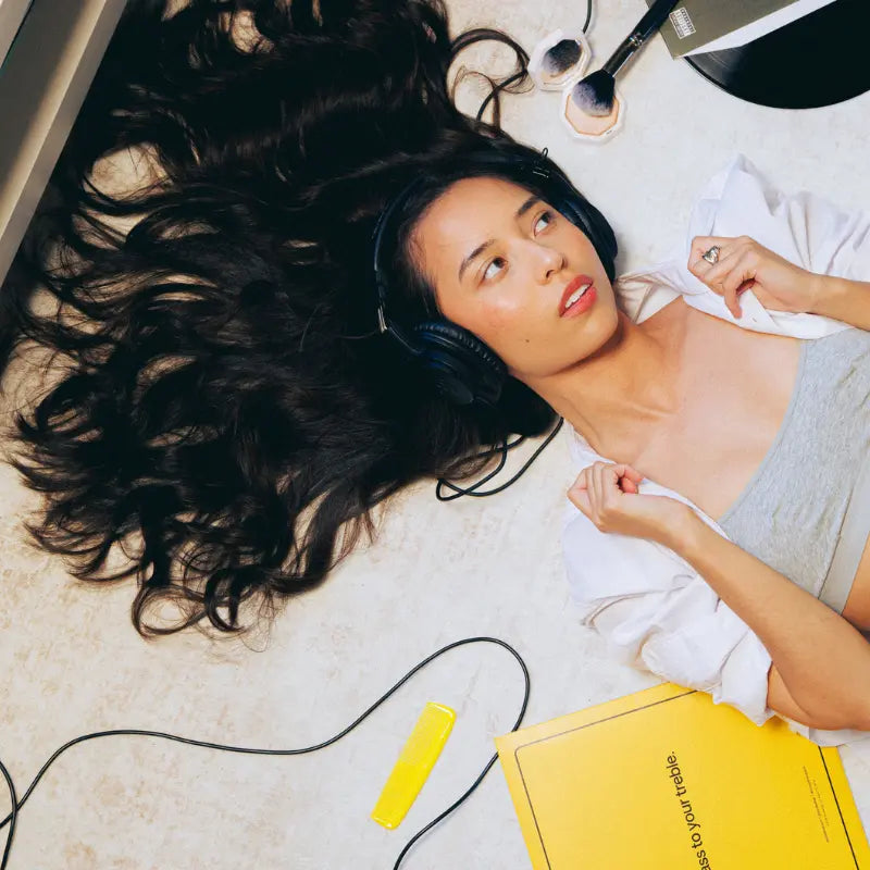 Vrouw met een koptelefoon ligt op de grond met haar lange donkere haar uitgewaaierd om haar hoofd