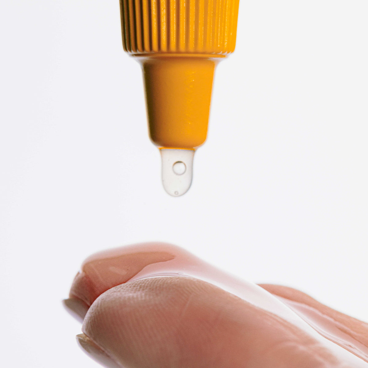 Druppel hangt aan een gele tuit boven een vinger met doorzichtige gel